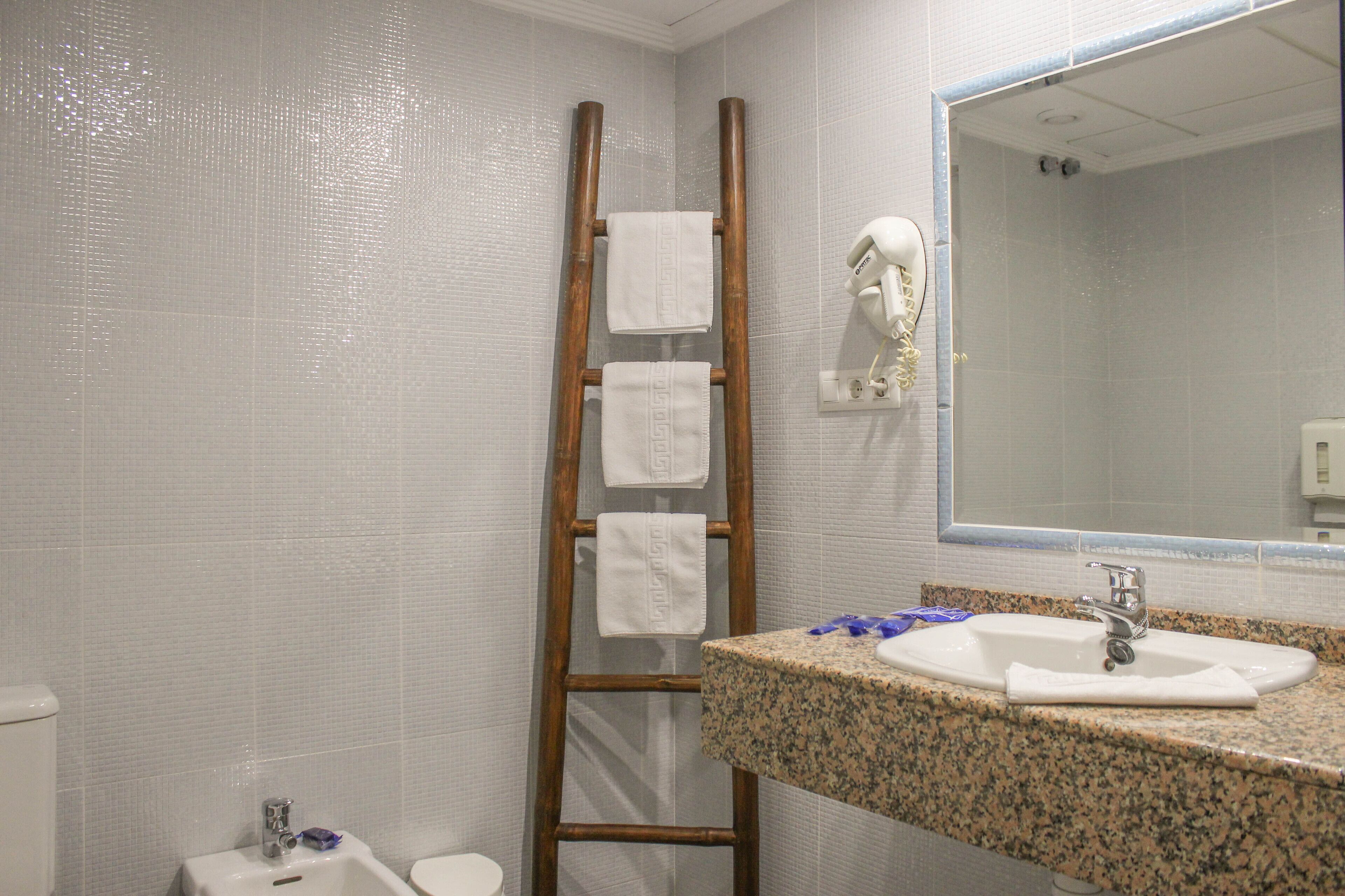 A bathroom with a granite countertop sink, a wooden ladder with towels, a handheld showerhead, and a mirror.