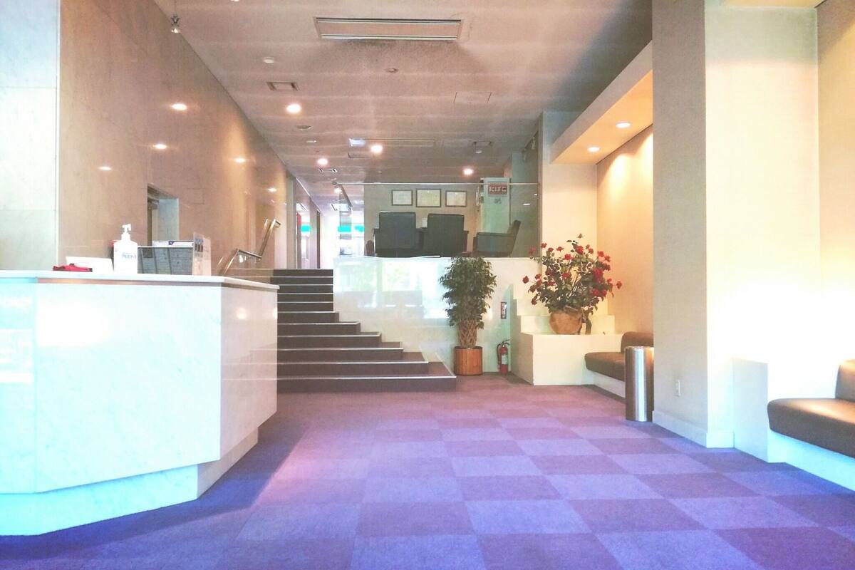 A reception area with a checkered floor, a reception desk, a staircase, and potted plants.