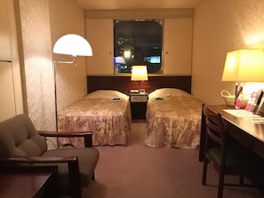 A hotel room with two beds, a desk, a chair, a lamp, and a window with a city view. - Hotel Satoh Tokyo (Tokyo)