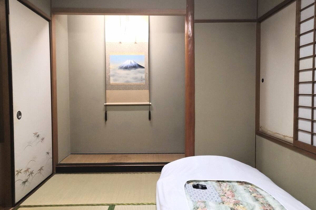 A traditional Japanese room with tatami flooring, a bed with a floral bedspread, a shoji screen with a mountain painting, and a sliding door with a bamboo design.
