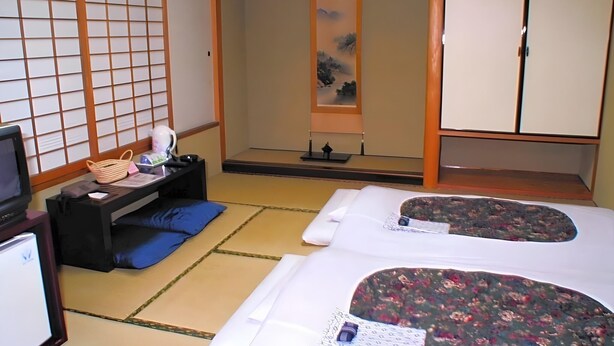 A traditional Japanese room with tatami flooring, a futon bed, a desk with a lamp, a television, and sliding doors. - Hotel Satoh Tokyo (Tokyo)