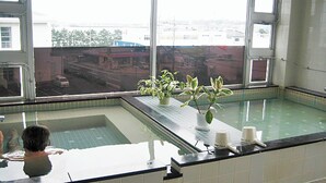 Zona de piscina con vistas a edificios, plantas en macetas al borde y suelo de baldosas.
