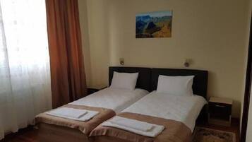 A hotel room with two beds, a painting on the wall, and a window with curtains.