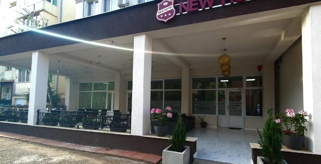 Entrada de hotel con zona de estar al aire libre techada, plantas en macetas y vista despejada del interior a través de puertas de vidrio.