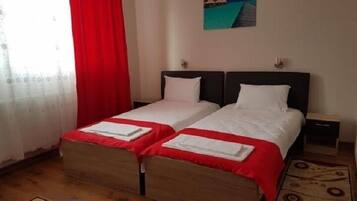 A hotel room with two beds, a red curtain, a painting, and a wooden floor.