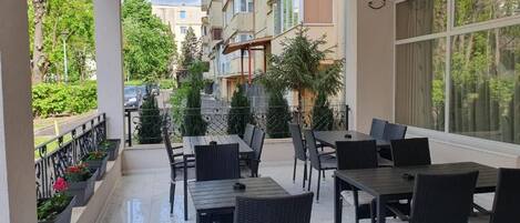 An outdoor patio with tables and chairs, a view of the street, and a building in the background.
