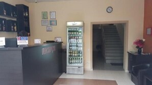 A reception area with a counter, a refrigerator stocked with beverages, framed certificates on the wall, and a clock. - Hotel New (Baia Mare)