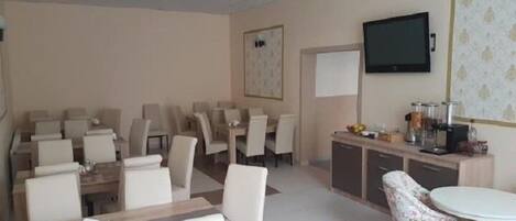 A hotel room with a dining area, a television mounted on the wall, and a small kitchenette.