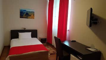 Una habitación de hotel con cama, escritorio, silla, mesita, televisor de pared y un cuadro en la pared.