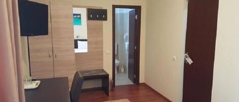 A hotel room with a bed, a desk, a TV, a wardrobe, and a bathroom door.