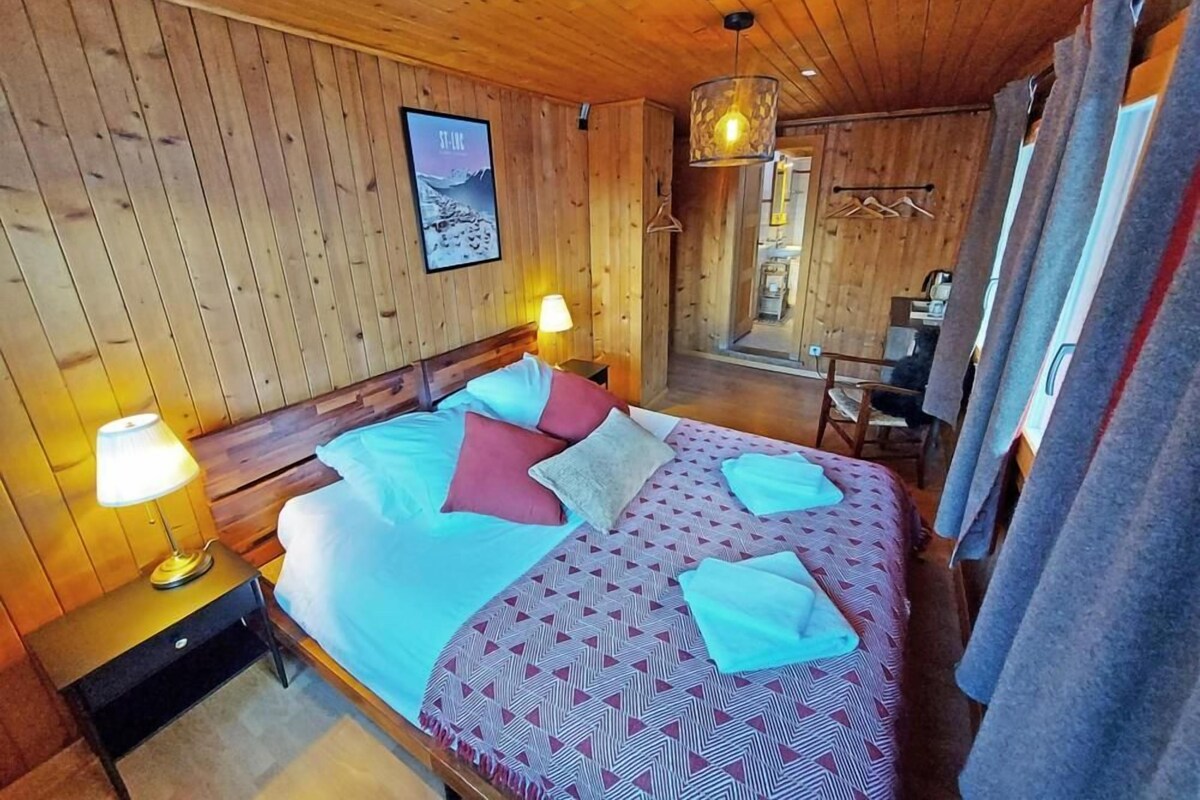 Una habitación de madera con una cama, dos lámparas de noche, un candelabro colgante y un cartel en la pared.
