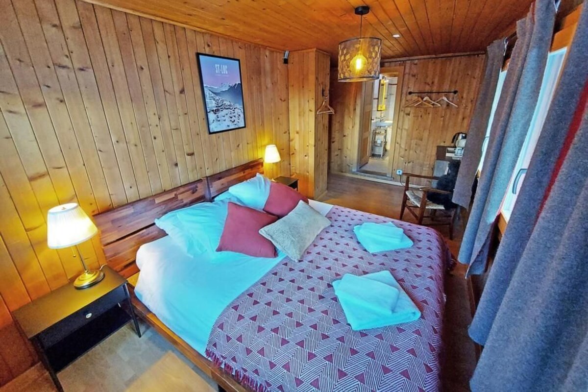 A wooden room with a bed, a nightstand, a lamp, a hanging light fixture, and a framed picture on the wall.