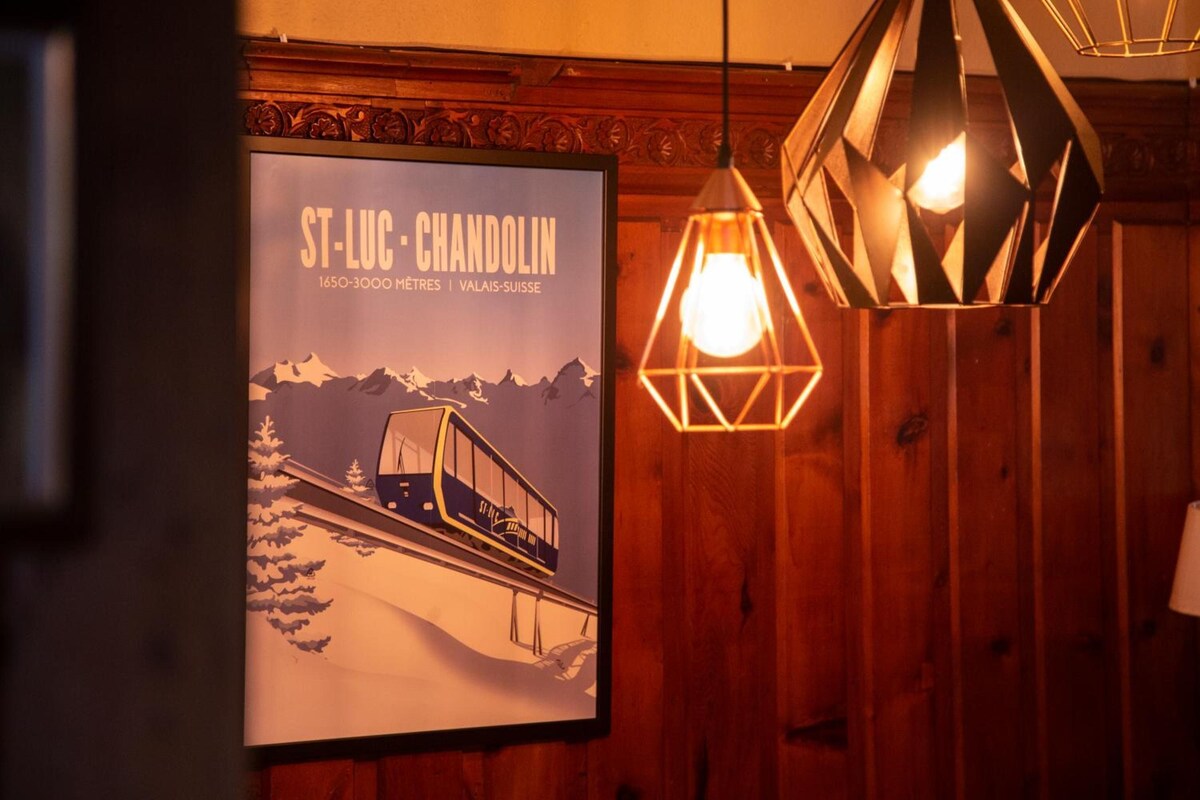 A poster of a mountain train with the text 'ST-LUC - CHANDOLIN 1650-3000 METRES | VALAIS-SUISE' and two hanging geometric light fixtures.