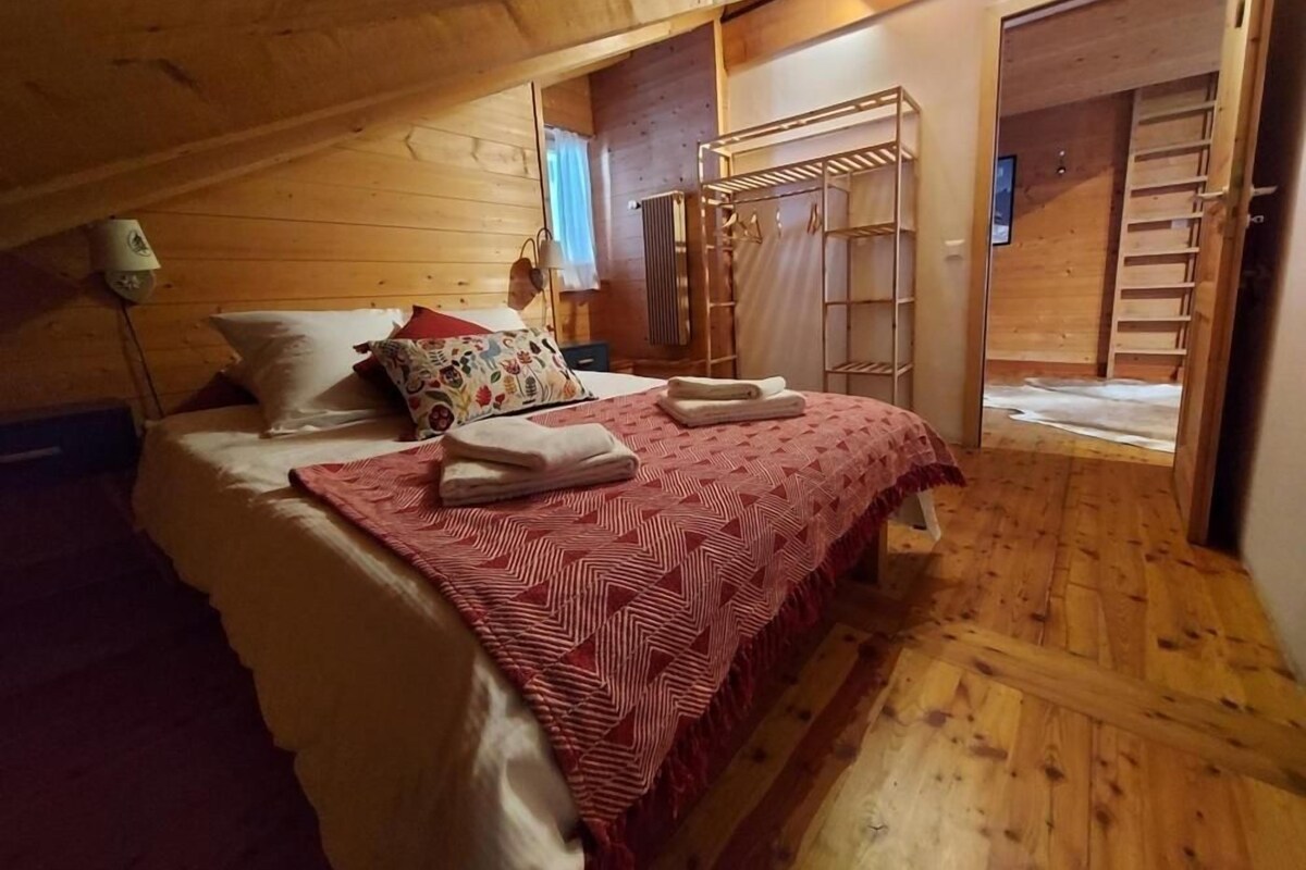 Un dormitorio acogedor con techo de madera, una cama con colcha estampada roja, una escalera de madera y un armario de madera.
