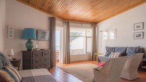 A cozy room with a wooden ceiling, a bed with striped bedding, a wicker chair, a sofa with cushions, a small table with a lamp, and a view of the outside through a window. - A29 - Calheta House in Luz by DreamAlgarve (Lagos)