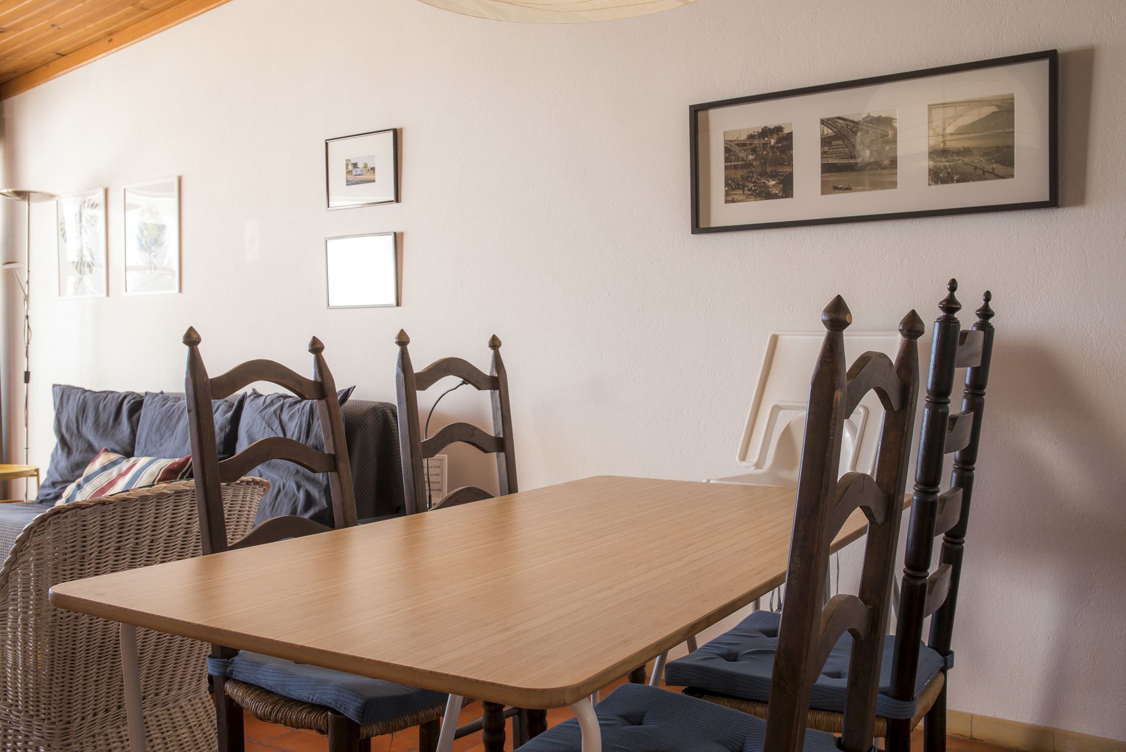 A dining area with a wooden table and chairs, framed pictures on the wall, and a wicker chair.