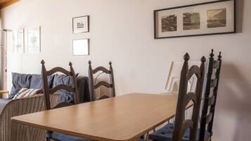 A dining area with a wooden table and chairs, framed pictures on the wall, and a wicker chair.