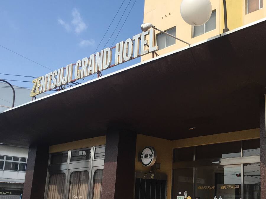 The exterior of the Zentsuji Grand Hotel with a clear sign, a clock, and a visible entrance.