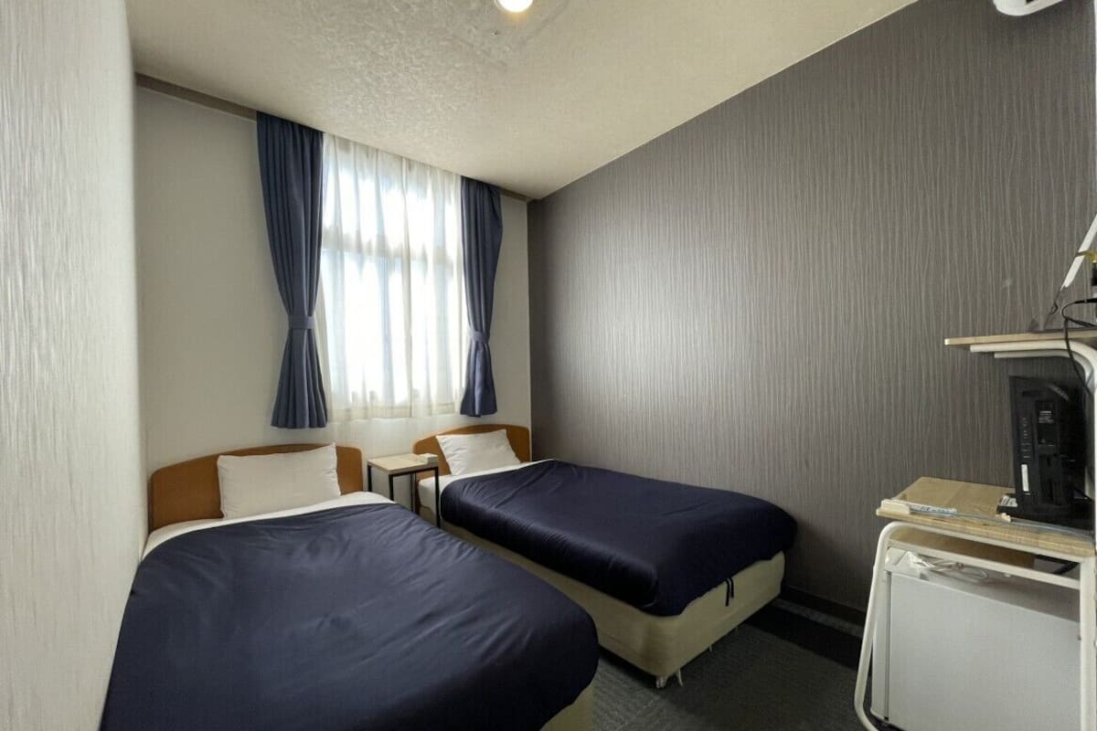 A hotel room with two beds, a desk, a chair, and a small kitchenette.