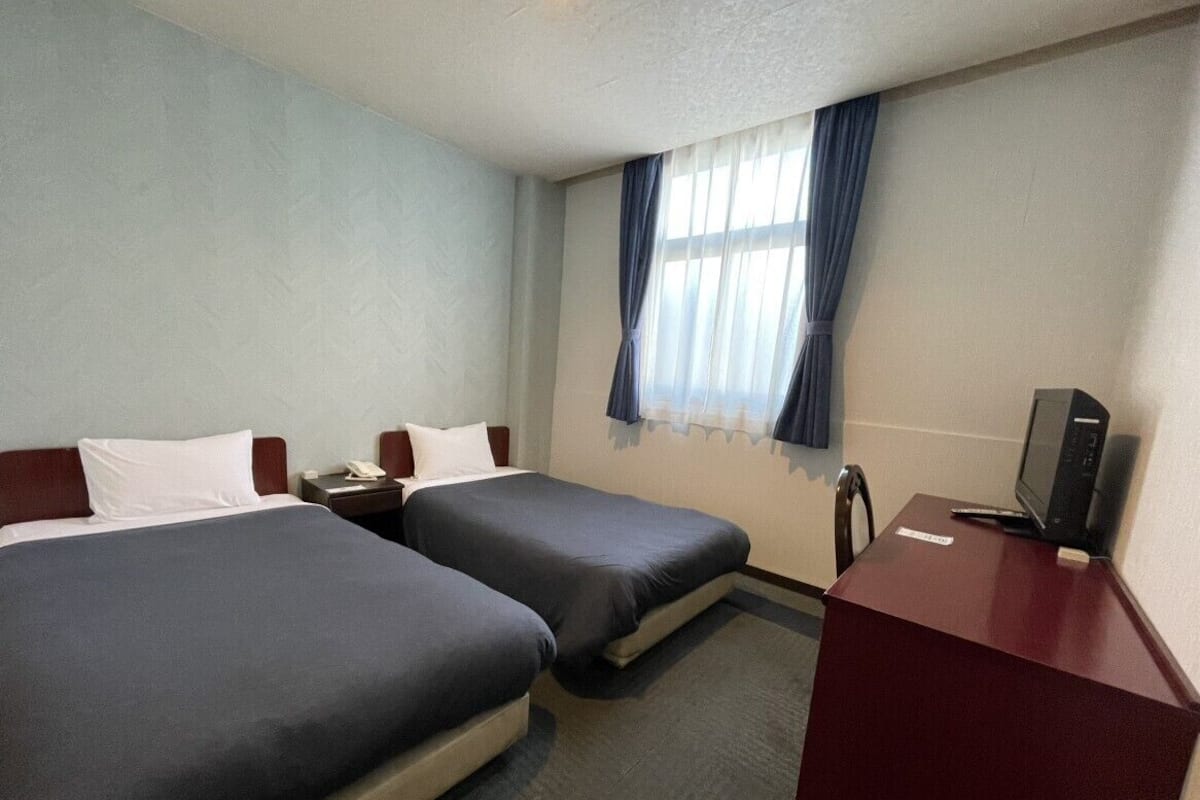 A hotel room with two beds, a desk with a computer, and a window with curtains.