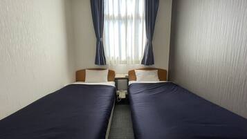 Hotellihuone, jossa on kaksi erillistä sänkyä, pieni yöpöytä ja ikkuna, jossa on verhot.
