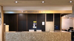 Un comptoir d’accueil avec une pancarte indiquant « SERVICE D’INFORMATION » et un petit tabouret en bois placé devant.