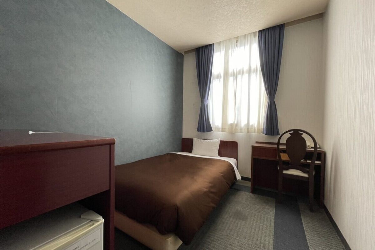 A hotel room with a bed, a desk, a chair, and a small table.