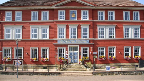 A red building with a central entrance, multiple windows, and flower boxes. - Double room 01 - Hotel Goldene Krone (Clausthal-Zellerfeld)