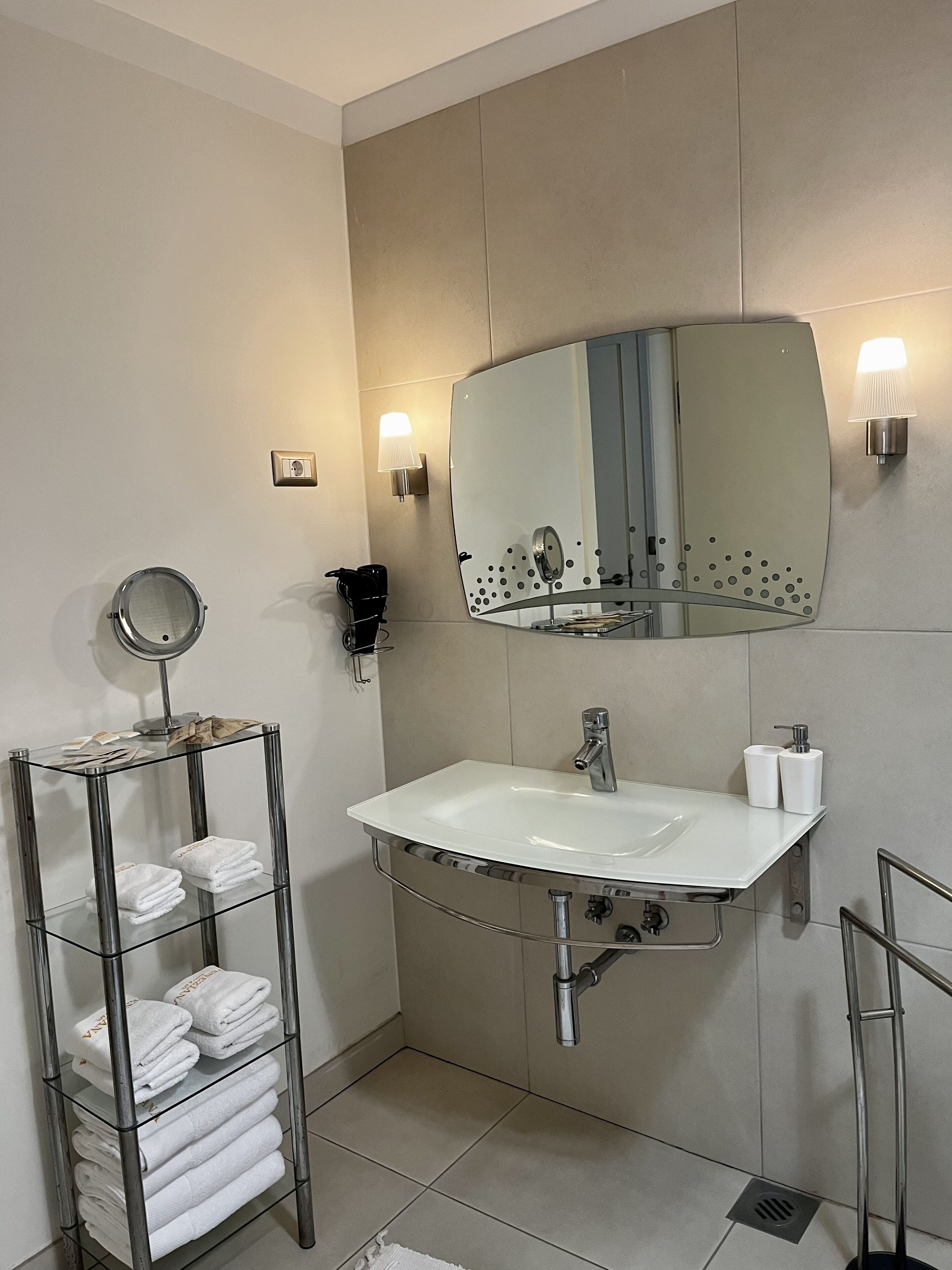 A modern bathroom with a white sink, a round mirror, and a towel rack with neatly folded towels.