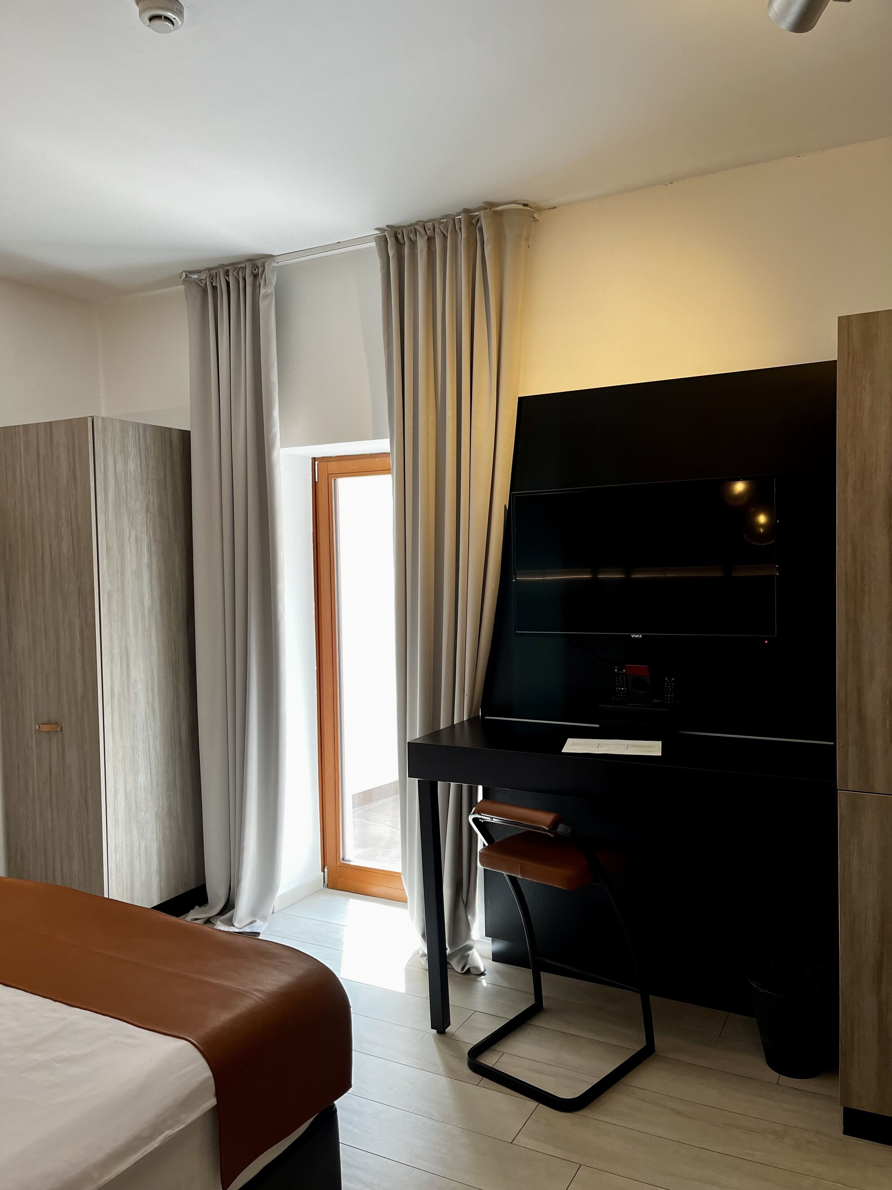 Une chambre d’hôtel moderne équipée d’un lit, d’un bureau avec une chaise, d’une télévision et d’une armoire.