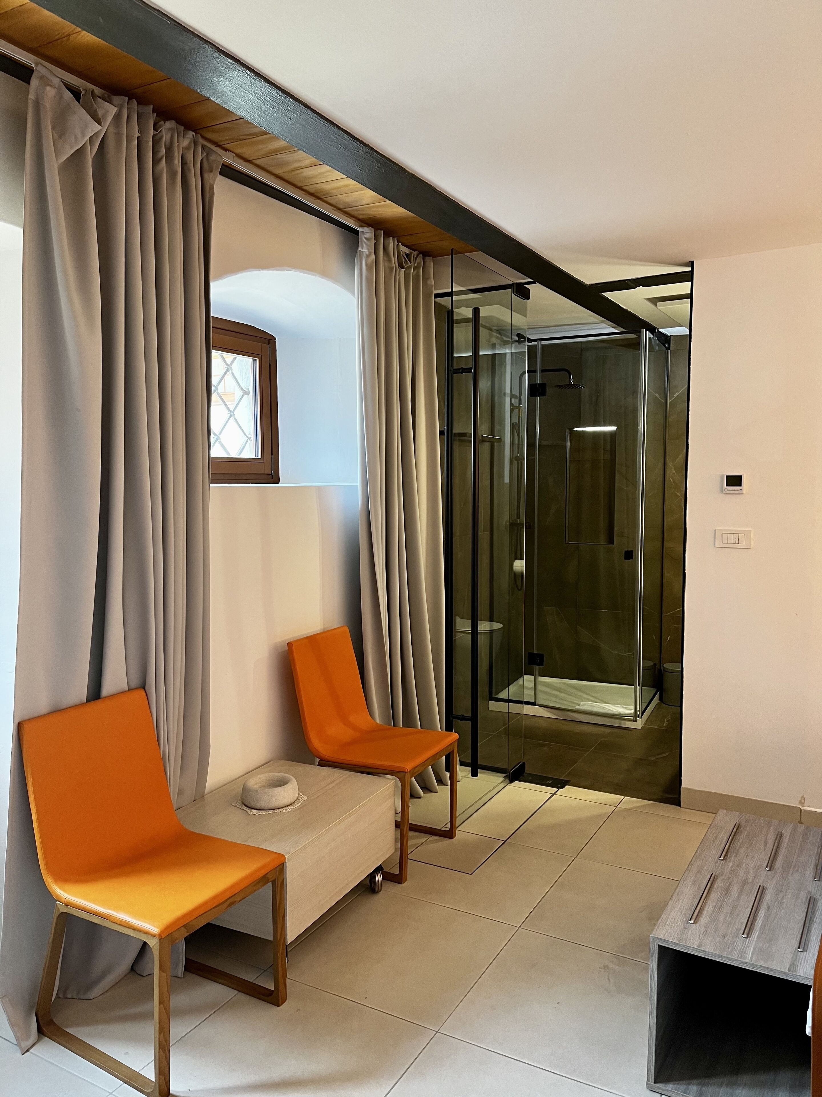 Un baño moderno con cabina de ducha de vidrio, un banco y una mesita.