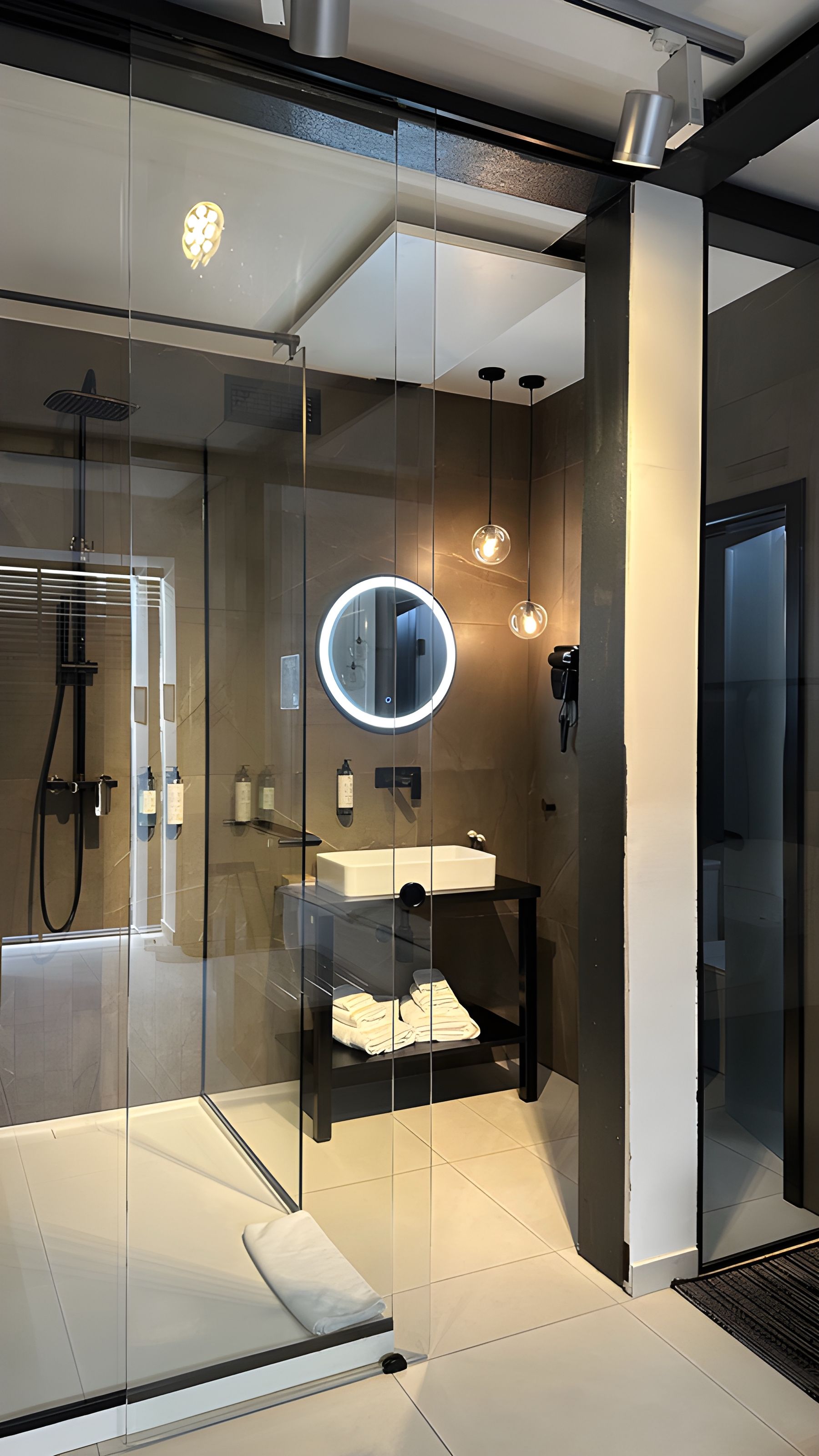 Un bagno moderno con pareti divisorie in vetro, uno specchio rotondo, un lavandino e una zona doccia.