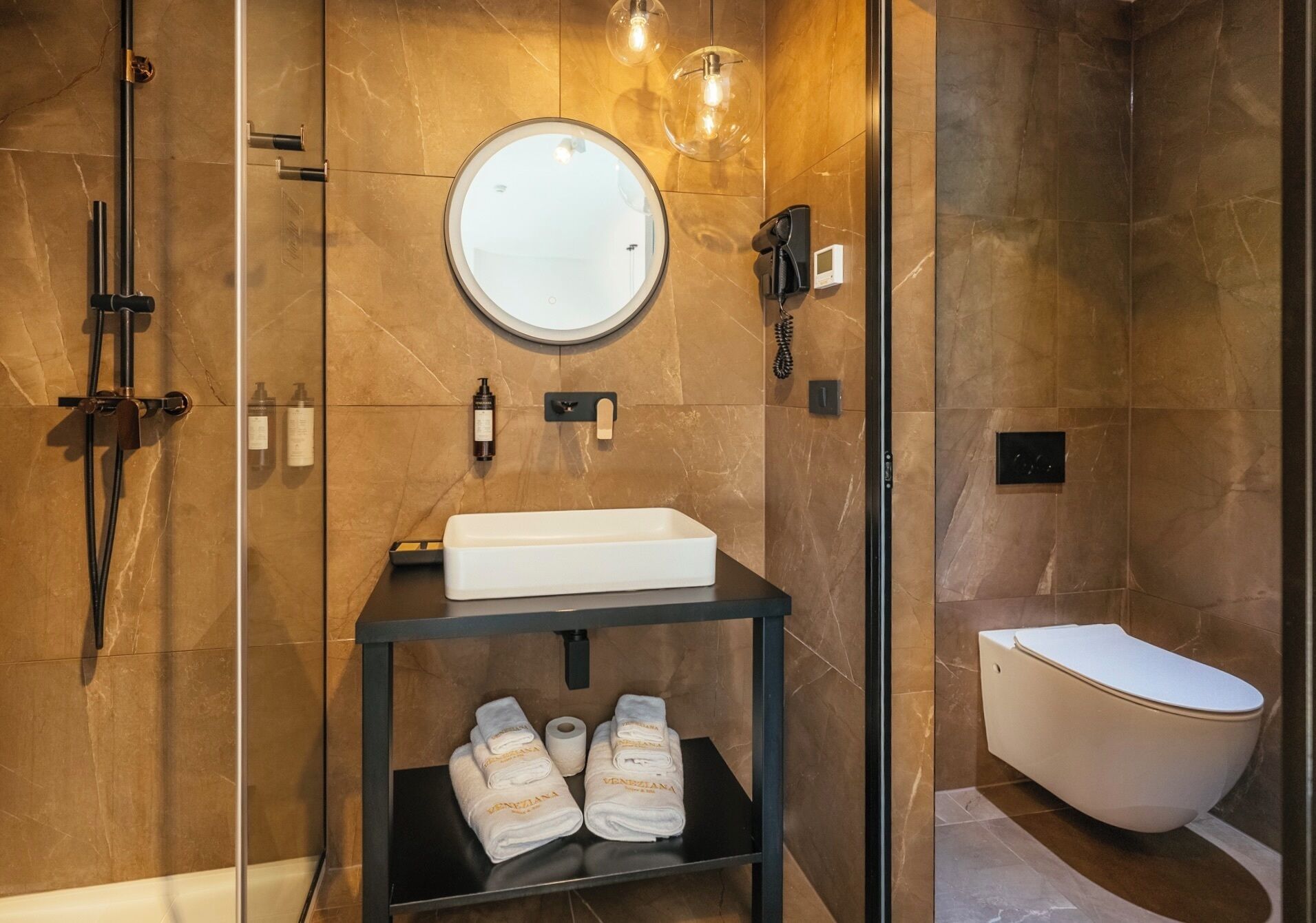 A modern bathroom with a built-in sink, a round mirror, a handheld showerhead, and a toilet.