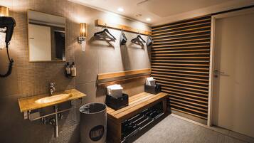 A modern bathroom with a sink, mirror, towel rack, bench, and a wall-mounted towel dispenser.