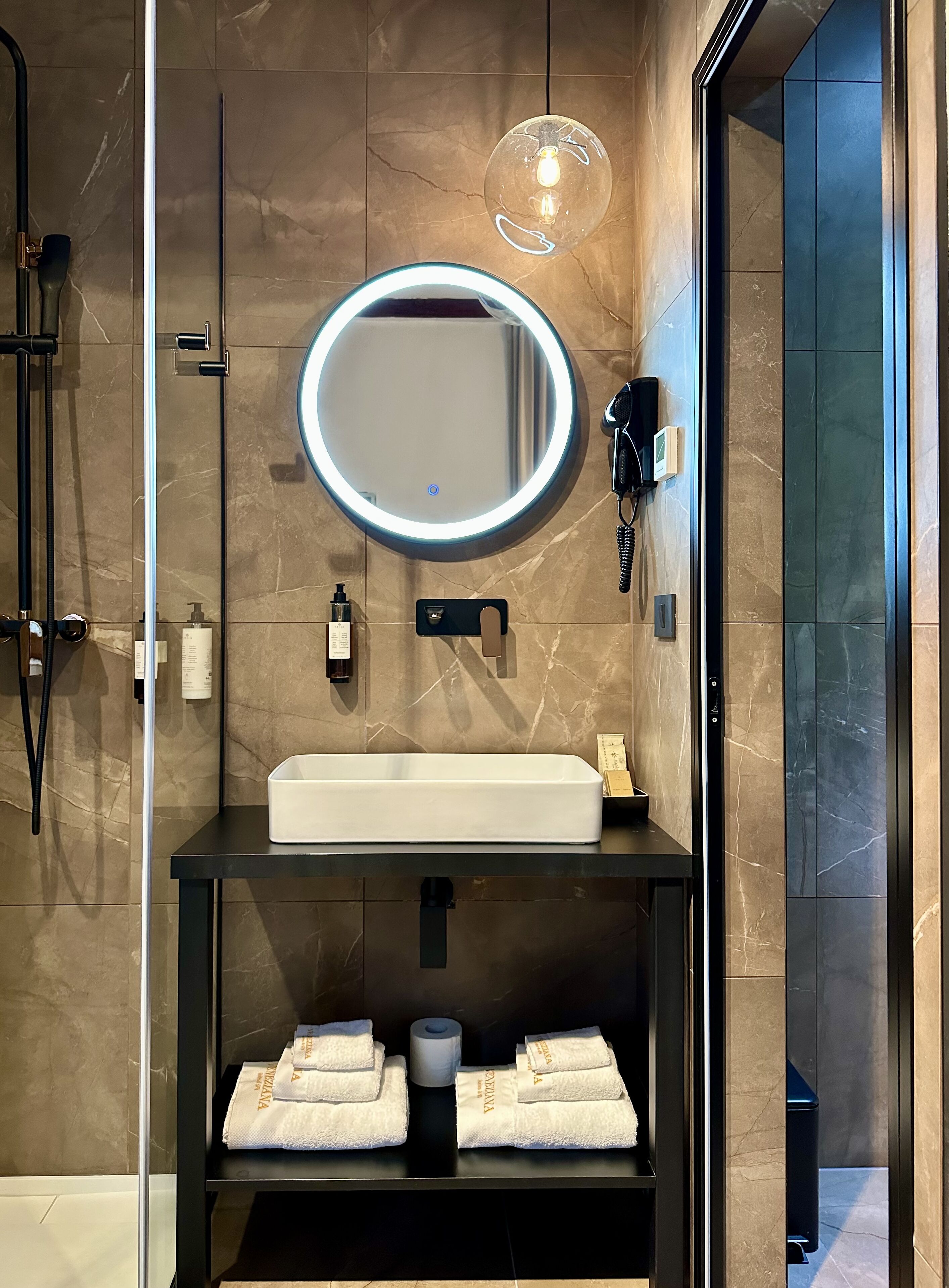 Un baño moderno con un espejo ovalado grande, un lavamanos rectangular y un perchero con toallas dobladas.