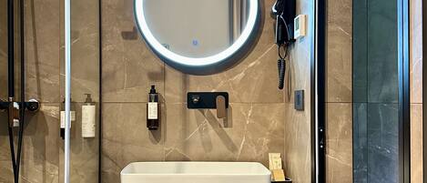 Un baño moderno con un espejo ovalado grande, un lavamanos rectangular y un perchero con toallas dobladas.