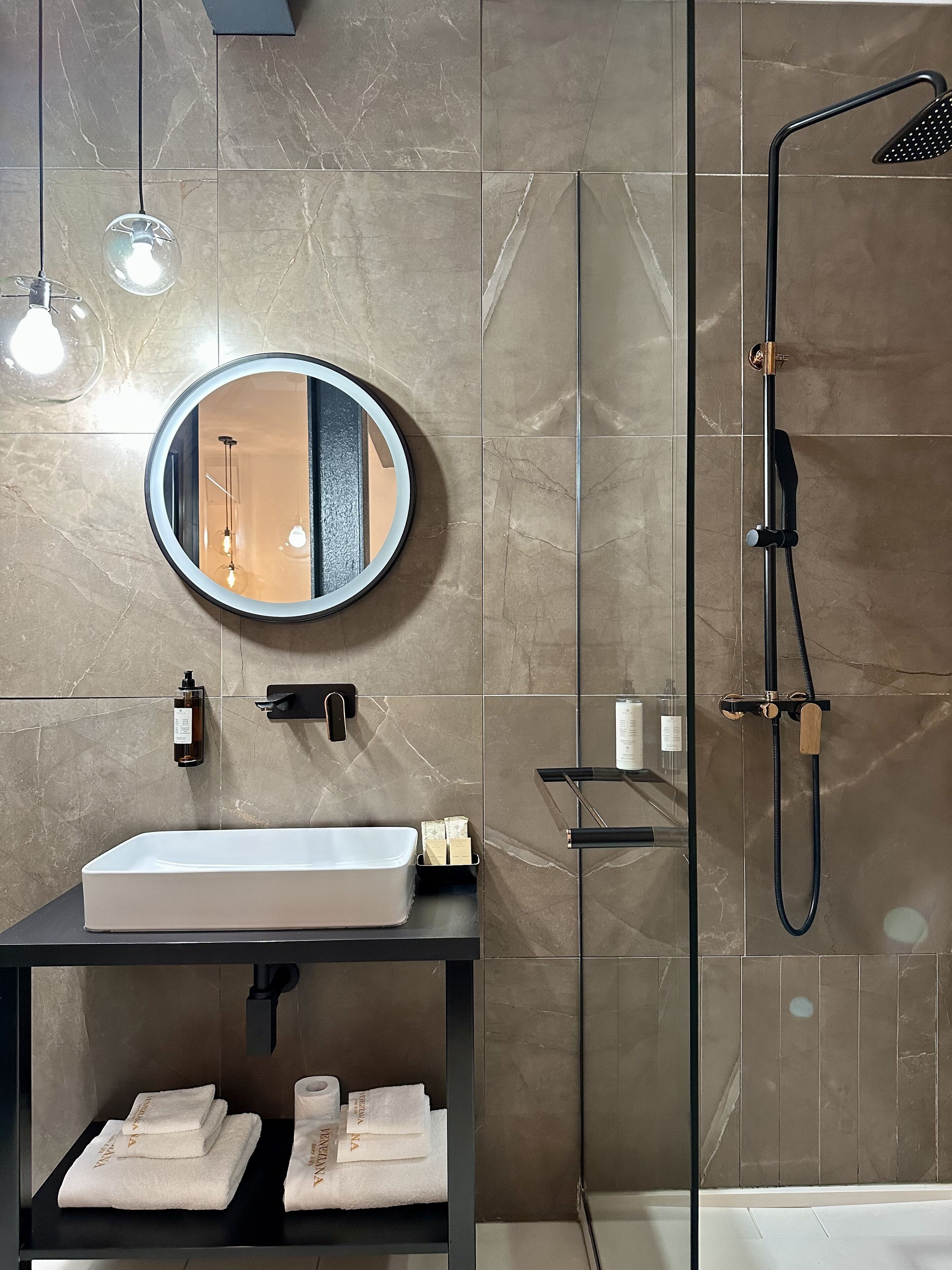 Un baño moderno con un lavamanos rectangular, un espejo redondo, un cabezal de ducha de mano y un perchero.