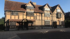 A traditional half-timbered house with a tiled roof, multiple windows with wooden frames, and a black metal fence in front. - Beautiful 2-bed Caravan in Stratford-upon-avon (Stratford-upon-Avon)