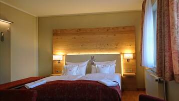 A hotel room with a wooden headboard, two bedside lamps, a red bedspread, and a window with curtains.