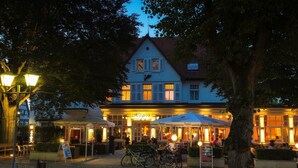 Un bâtiment de style européen traditionnel, avec un café et un restaurant au rez-de-chaussée, entouré d’arbres et doté d’une terrasse.