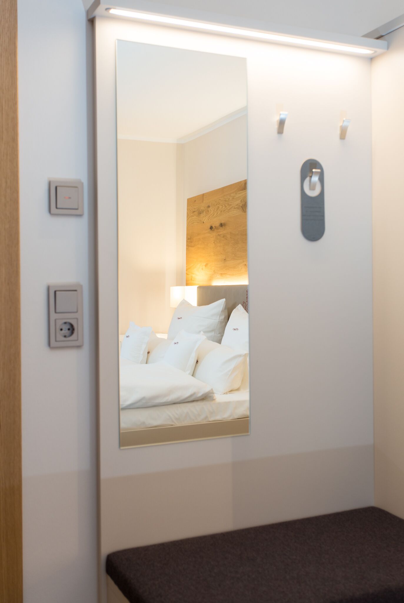 A hotel room with a large mirror, a bedside table, a wall-mounted light, and a wooden headboard.
