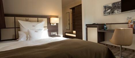 Una habitación de hotel con una cama grande, un escritorio, una silla y un espejo.