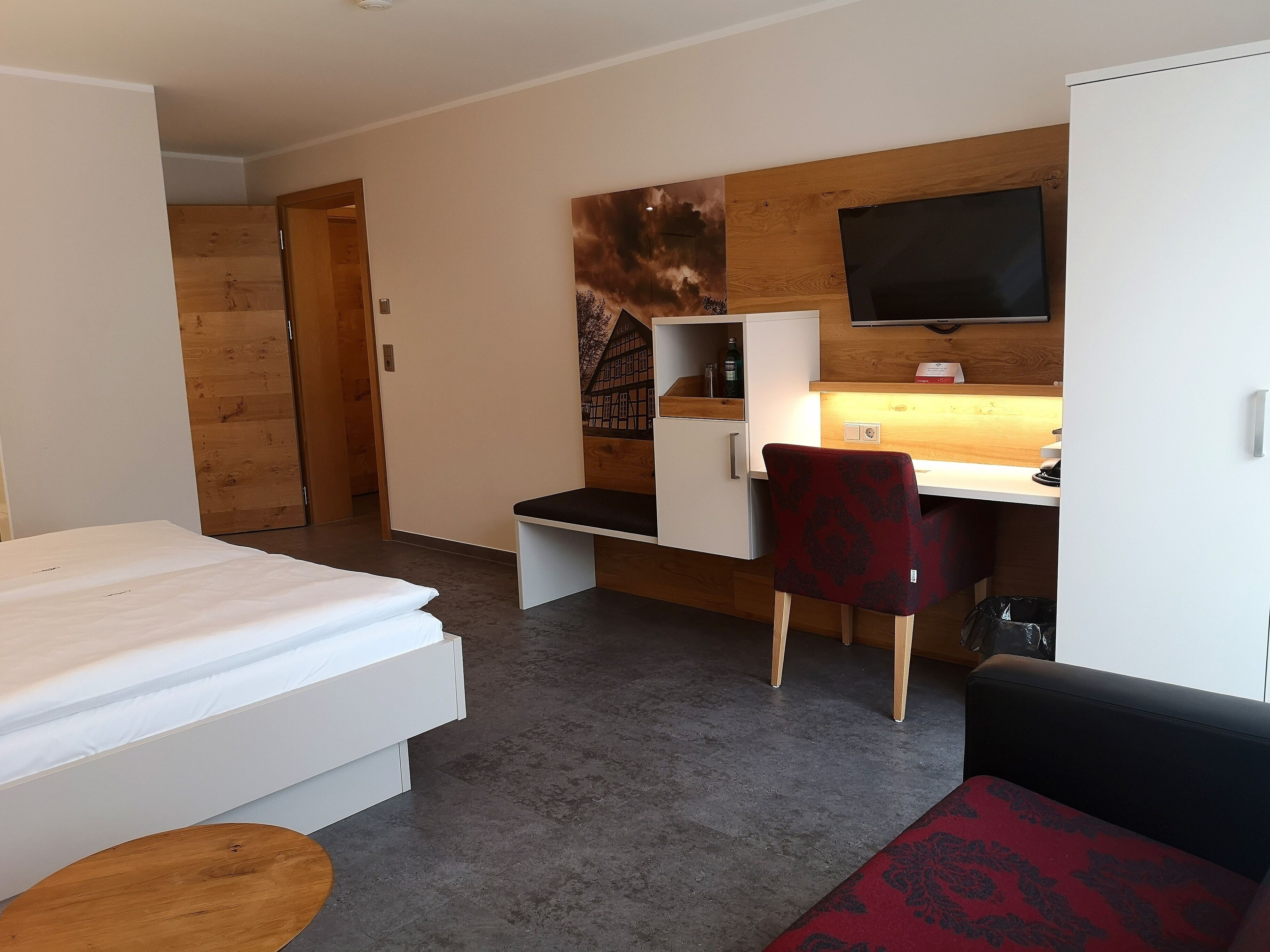 A hotel room with a bed, a desk with a chair, a TV, and a wardrobe.