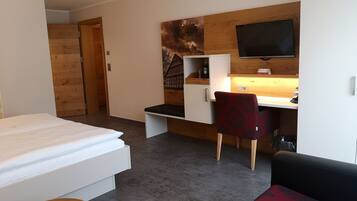 A hotel room with a bed, a desk with a chair, a TV, and a wardrobe.