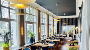 Un restaurant avec de longues tables et des chaises bleues, de grandes fenêtres et des lampes suspendues.