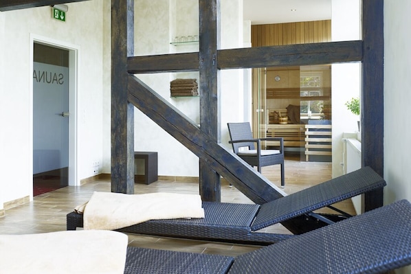 A modern interior with a wooden staircase, lounge chairs, and a visible bathroom with a towel rack.