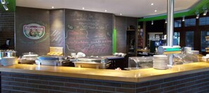 A buffet counter with a chalkboard menu, a logo on the wall, and a brick wall base. - Haus Deutsch Krone (Bad Essen)
