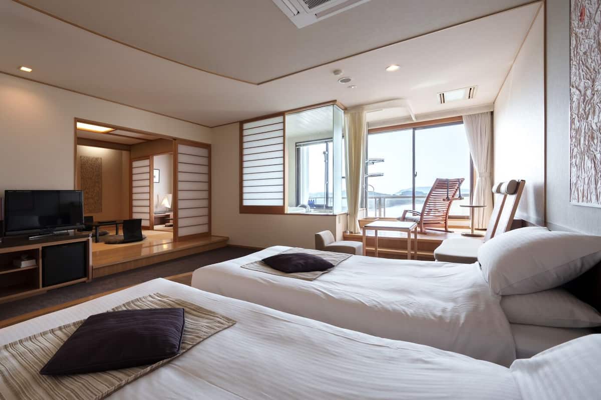 A hotel room with two beds, a TV, a desk, and a view of the outside.