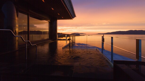 A waterfront terrace with a glass railing, a metal staircase, and a view of the sunset over the water. - Yuyawan Onsen Hotel Yokikan (Nagato)