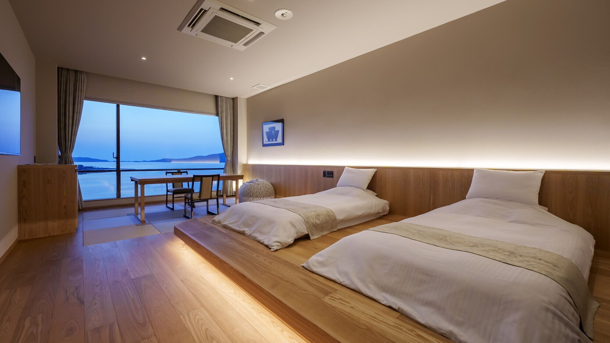 A hotel room with two beds, a desk, and a large window with a view.